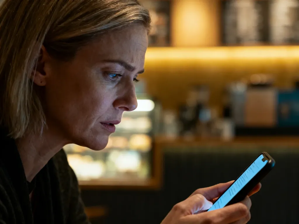 Zirytowana kobieta patrząca na ekran smartfona w kawiarni, co ilustruje problem z płatnością mobilną.